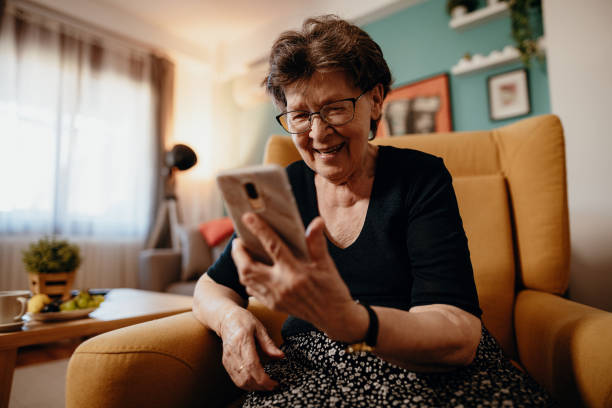 verticale de femme aînée à la maison utilisant le téléphone mobile et les technologies - seulement des femmes seniors photos et images de collection