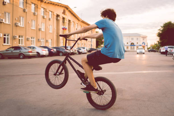joven montando en una bicicleta bmx en una rueda trasera trasera, haciendo trucos en la ciudad - bmx cycling cycling bicycle teenager fotografías e imágenes de stock