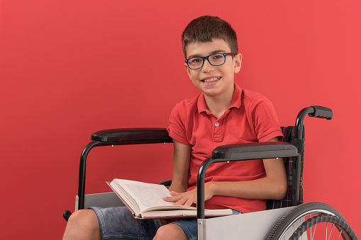 Disabled boy in wheelchair reading book colored background