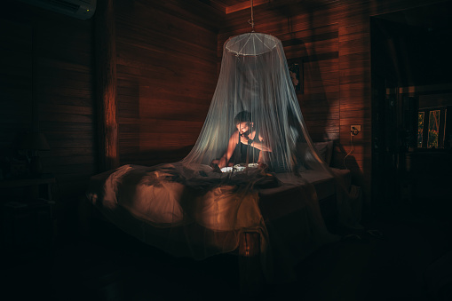 Man sitting on bed covered with mosquito net and reading