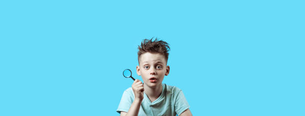 istock a boy in a light t-shirt holding a small magnifying glass on blue background 1168741692