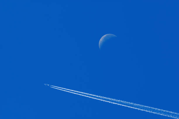 Flying commercial airliner passes by a crescent moon in a deep blue sky Flying commercial airliner passes by a crescent moon in a deep blue sky. Airtraffic, transportation, travel and weather concepts contrail moon on a night sky stock pictures, royalty-free photos & images