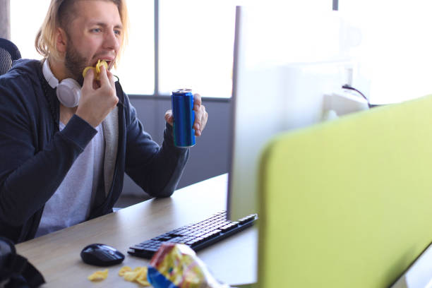 istock Concentrated young man in casual clothing using computer, streaming playthrough or walkthrough video and eating chips. 1168746025