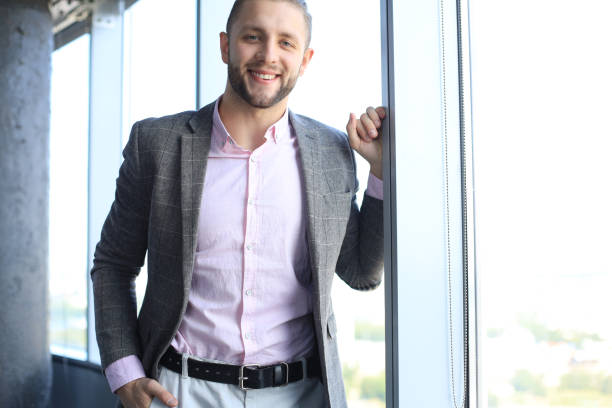 istock Smiling young business man looking at camera while standing near the window. 1168746868