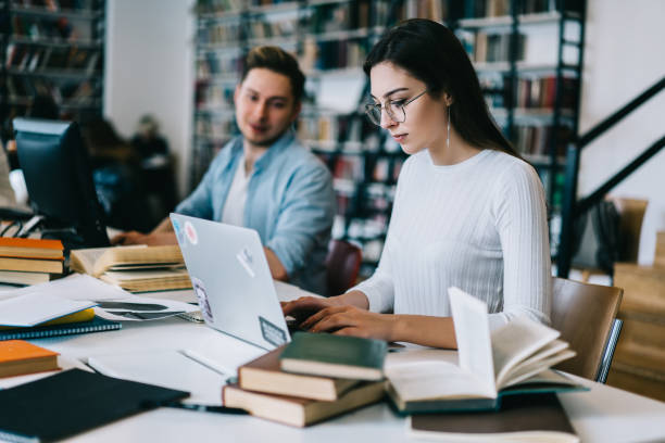 istock Concentrated female student typing on laptop computer creating report for homework in modern university library with wifi, young woman and man studying together in college campus using technology 1168752300