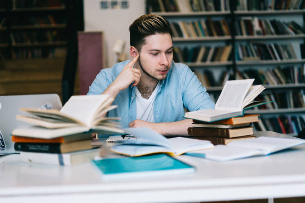 istock Pensive male student sitting at desktop learning information for university examination,clever hipster guy spending time on autodidact reading textbook and literature doing homework in library 1168752302