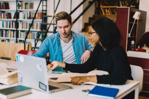 istock Multiracial male and female colleagues discussing olan of common coursework project sitting at desktop in campus using technology and wifi, hipsters talking while learning in library  together 1168752396