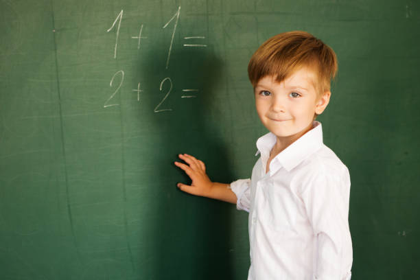 istock Boy writes chalk on blackboard. Schoolboy about a board solves examples. Back to school concept. 1168754730