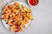 Sweet Chilli Shrimp Skewers with lemon and parsley on gray stone background