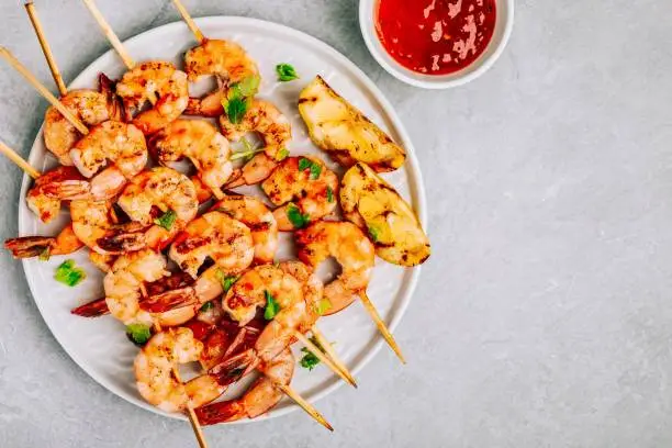 Sweet Chilli Shrimp Skewers with lemon and parsley on gray stone background, top view