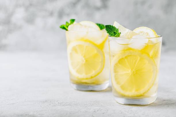 istock Lemonade with lemon, mint and ice cubes in glass on gray stone background. 1168757462
