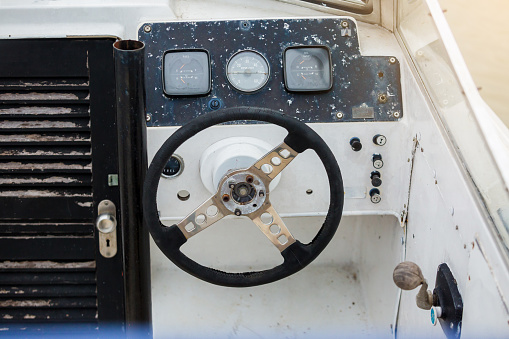 Old and damage steering wheel and dashboard of white speedboat. Damaged speedboat is parking on the river. White speedboat damaged.