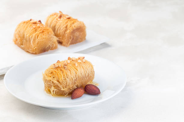 greek pastry kataifi with shredded filo dough stuffed with almond nuts, in honey syrup, on white plate, horizontal, copy space - central greece imagens e fotografias de stock