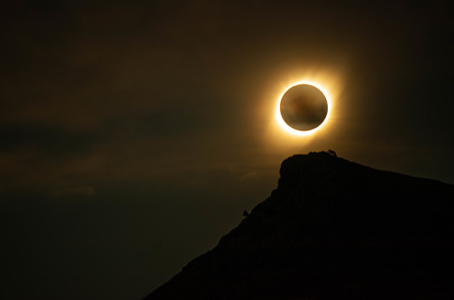 moon capping the sun in a solar eclipse over the top of a mountain