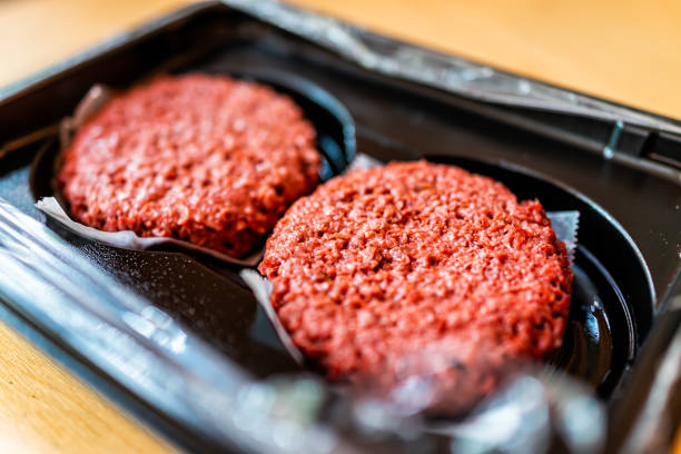 nahaufnahme von zwei rohen ungekochten roten veganen fleisch burger patties in kunststoffverpackungen - fleischersatz stock-fotos und bilder