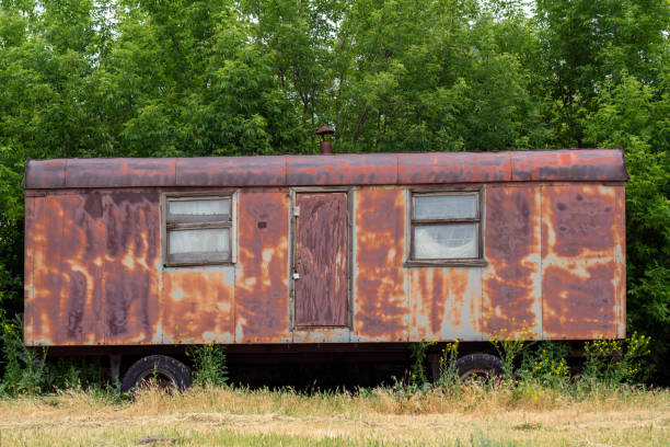 Photo of rusty abandoned metal van left in nature. Trees are seen on the backgraound. No people are seen in the frame. Shoot under daylight.