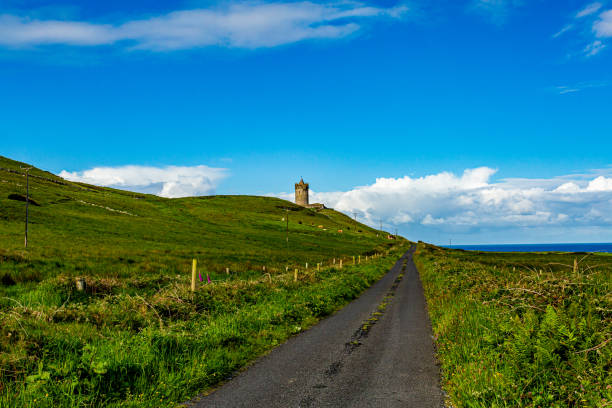 Beautiful landscape of a road between the Irish countryside with the Doonagore Castle tower in the background stock photo