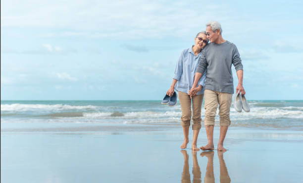 edad, viajes, turismo y concepto de personas - feliz pareja mayor que se está tomando de la mano y caminando en la playa de verano - couple human hand holding walking fotografías e imágenes de stock