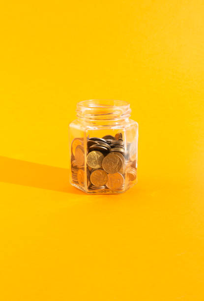 coins in transparent glass jar on orange background coins in transparent glass jar on orange background deposit bottle stock pictures, royalty-free photos & images