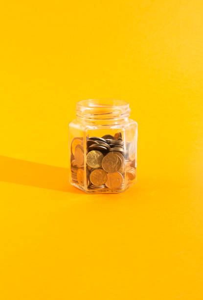 monety w przezroczystym szklanym słoiku na pomarańczowym tle - jar penny coin currency zdjęcia i obrazy z banku zdjęć