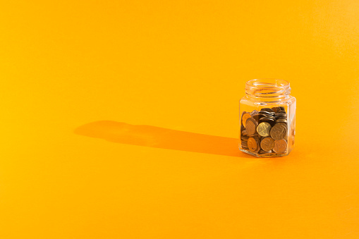 coins in transparent glass jar on orange background