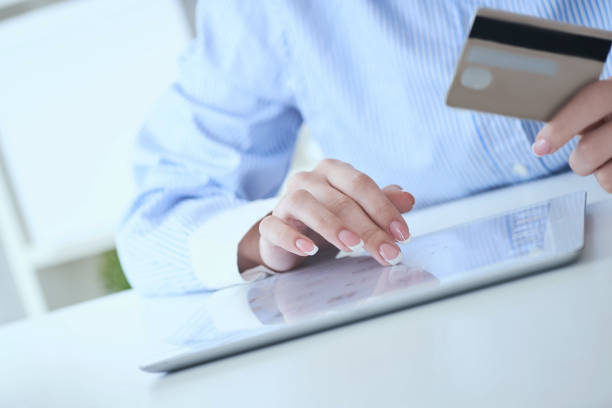 istock Close-up woman's hands holding a credit card and using tablet pc for online shopping. Middle section of young businesswoman making online payments with credit card and tablet. 1168781733