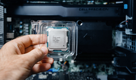 Paris, France - May 31, 2019: Front view of engineer male hand holding new professional Intel Xeon E5-2687w v4 CPU processor in plastic blister unboxing with Dell Precision Workstation in background