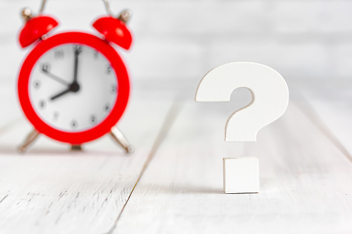 Question mark with alram clock on white wood table over white brick background with copy space.