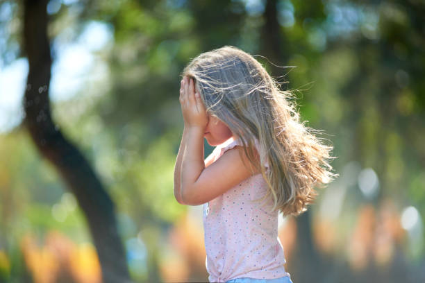 close-up portrait of a sad little girl sitting on the field in the grass at sunset looking at camera