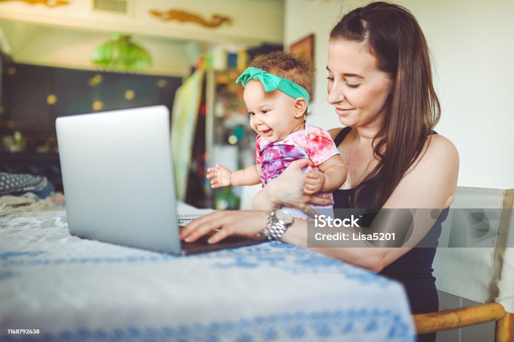 Madre y bebé se senten frente a un ordenador portátil en casa, trabajando, videochat o telemedicina - Foto de stock de Madre libre de derechos