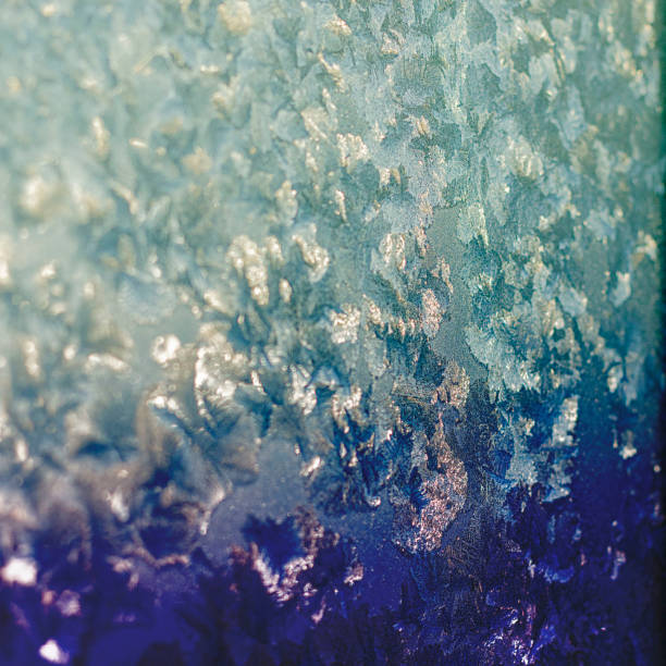 istock Ice patterns on winter glass of window, with the light seen through it. Light blue duotone. Square. Selective focus. Creative background about winter, cold, christmas time. 1168793400