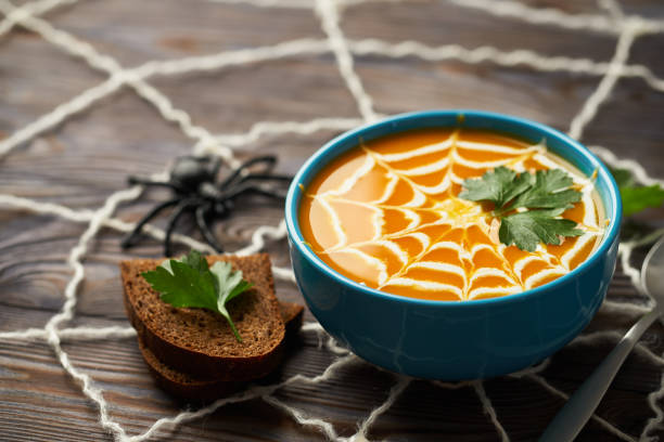 A healthy pumpkin puree garnished with cream and parsley leaves. Composition autumn cream soup with toys for the holiday Halloween on a dark wooden background stock photo