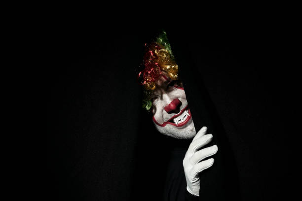 istock A terrible scary clown in a colored wig peeps out from behind black curtains. 1168800600