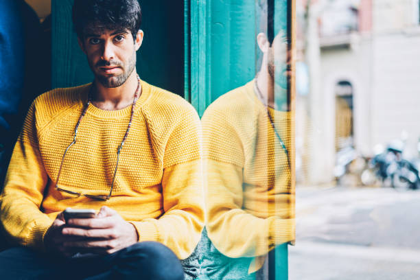 istock Portrait of bearded young man with eyeglasses on neck looking at camera while checking email on smartphone and installing mobile application.Male chatting online on phone via internet connection 1168817185
