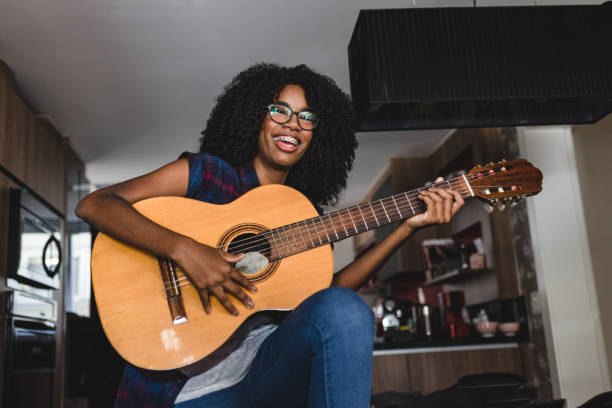 ragazza adolescente sorridente che tiene in mano una chitarra acustica a casa - plucking an instrument foto e immagini stock