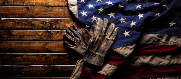 Old and worn work gloves on large American flag - Labor day background Old and worn work gloves on large American flag - Labor day background labor union stock pictures, royalty-free photos & images