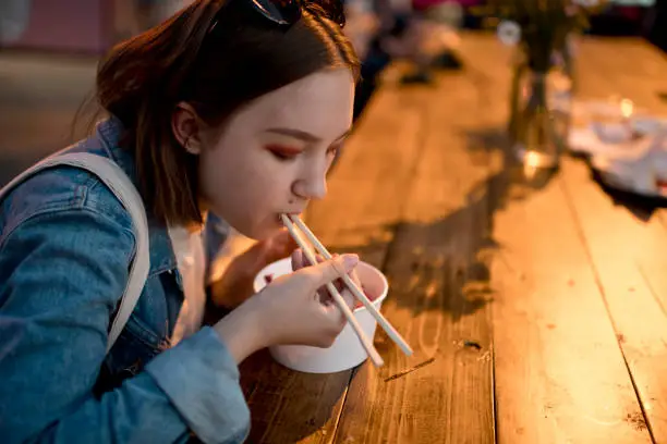 Teenage girl eating Asian food in a food festival