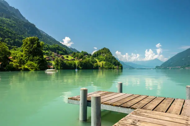 View of Brienz lake with clear turquoise water. Wooden pier. Traditional wooden houses on the shore of Brienz lake in the village of Iseltwald, Switzerland