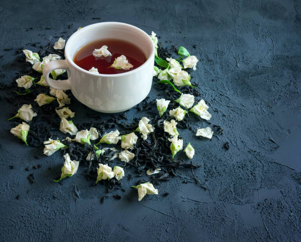 thé noir avec le jasmin dans une tasse sur un fond textural, avec le thé sec saupoudré autour et les fleurs sèches de jasmin - jasmine tea black tea tea drink photos et images de collection