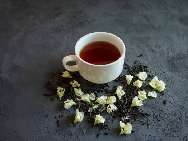 thé noir dans une tasse blanche sur un fond textural, avec le thé sec saupoudré autour et les fleurs sèches de jasmin - jasmine tea black tea tea drink photos et images de collection