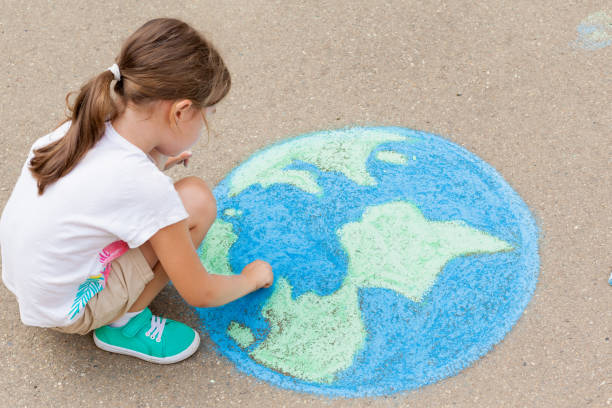 the  child girl draws a planet of the world with colored chalk on the asphalt. children's drawings, paintings and concepts. education and art, be creative when you return to school.  earth, peace day - child chalking imagens e fotografias de stock