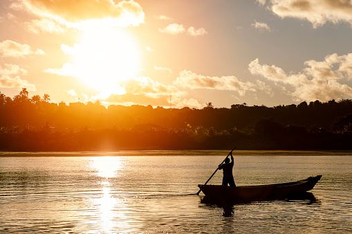 Fisherman rowing on a small canoe by sunset in Caraíva river, Bahia, Northeastern Brazil. DSLR Canon Mark IV
