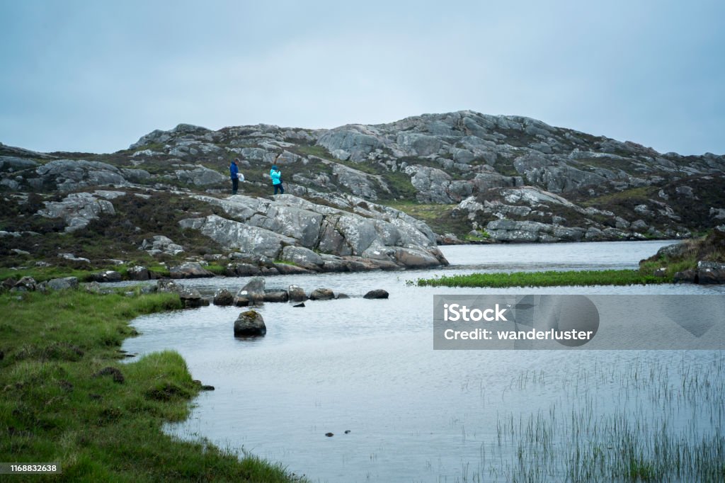 Narnia endpoint on the hike past ancient watermills on Lewis Island Two distant hikers reach Narnia, a place of tranquil beauty on the trail past ancient Norse watermills, is a small loch or lake surrounded by rocks, Valtos, Lewis Island, Outer Hebrides, Scotland, UK Adult Stock Photo