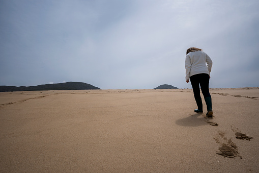 Solo female tourist walks up a sand dune to reach Sgarasta Bheag, Scaristaveg Beach, Harris, Isle of Lewis, Outer Hebrides, Scotland, UK, Europe
