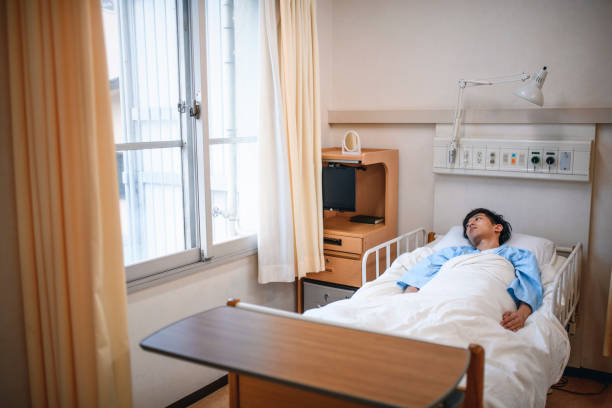 病院のベッドに横たわる深刻な若い男性日本人患者 - 入院 日本人 ストックフォトと画像