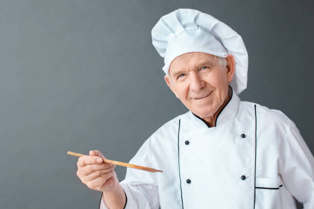 istock Senior chef studio standing isolated on gray holding spatula looking camera positive close-up 1168842425