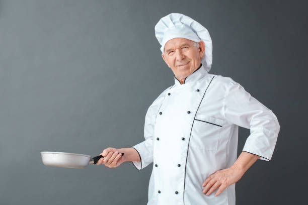 istock Senior chef studio standing isolated on gray holding pan posing looking camera happy 1168842429