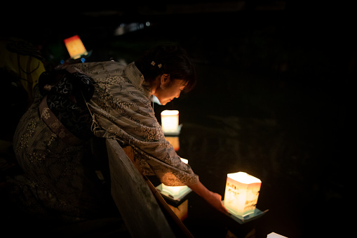 Japanese woman in yukata releasing paper lantern for toro nagashi event in summer Japan