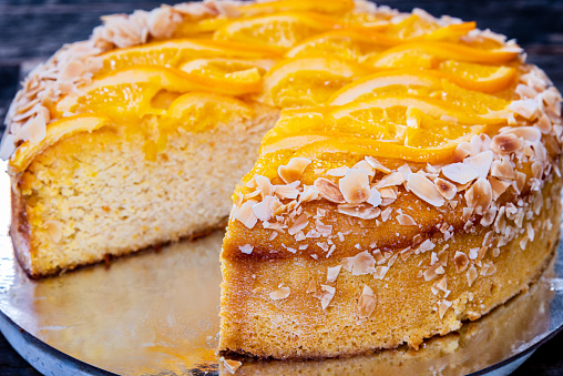 An orange cake on a silver platter, covered with slivered almonds and sliced pieces of orange
