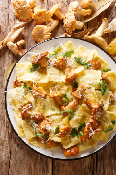 Pasta ravioli with fried chanterelles and parmesan cheese close-up on a plate. Vertical top view Pasta ravioli with fried chanterelles and parmesan cheese close-up on a plate on the table. Vertical top view from above chanterelle edible mushroom gourmet uncultivated stock pictures, royalty-free photos & images